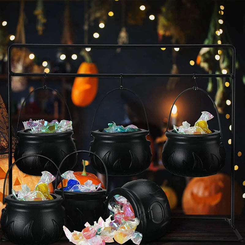 Black cauldron-shaped candy holders with Halloween-themed treats on a decorative stand.