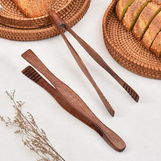 Wooden bread knives on a white surface with bread and wicker baskets in the background.