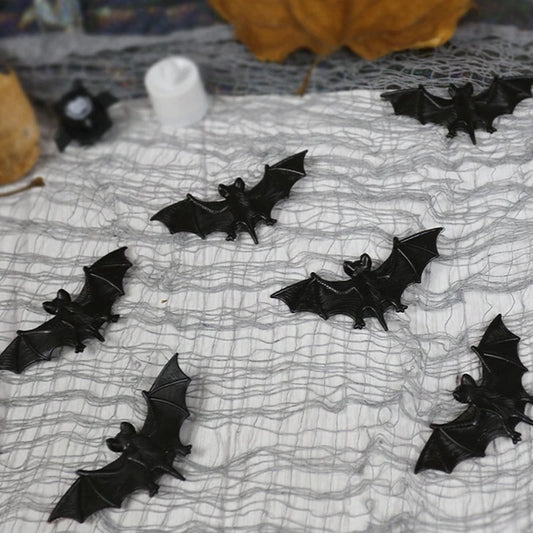 Black decorative bats on a spider web tablecloth with pumpkins and candles in the background.
